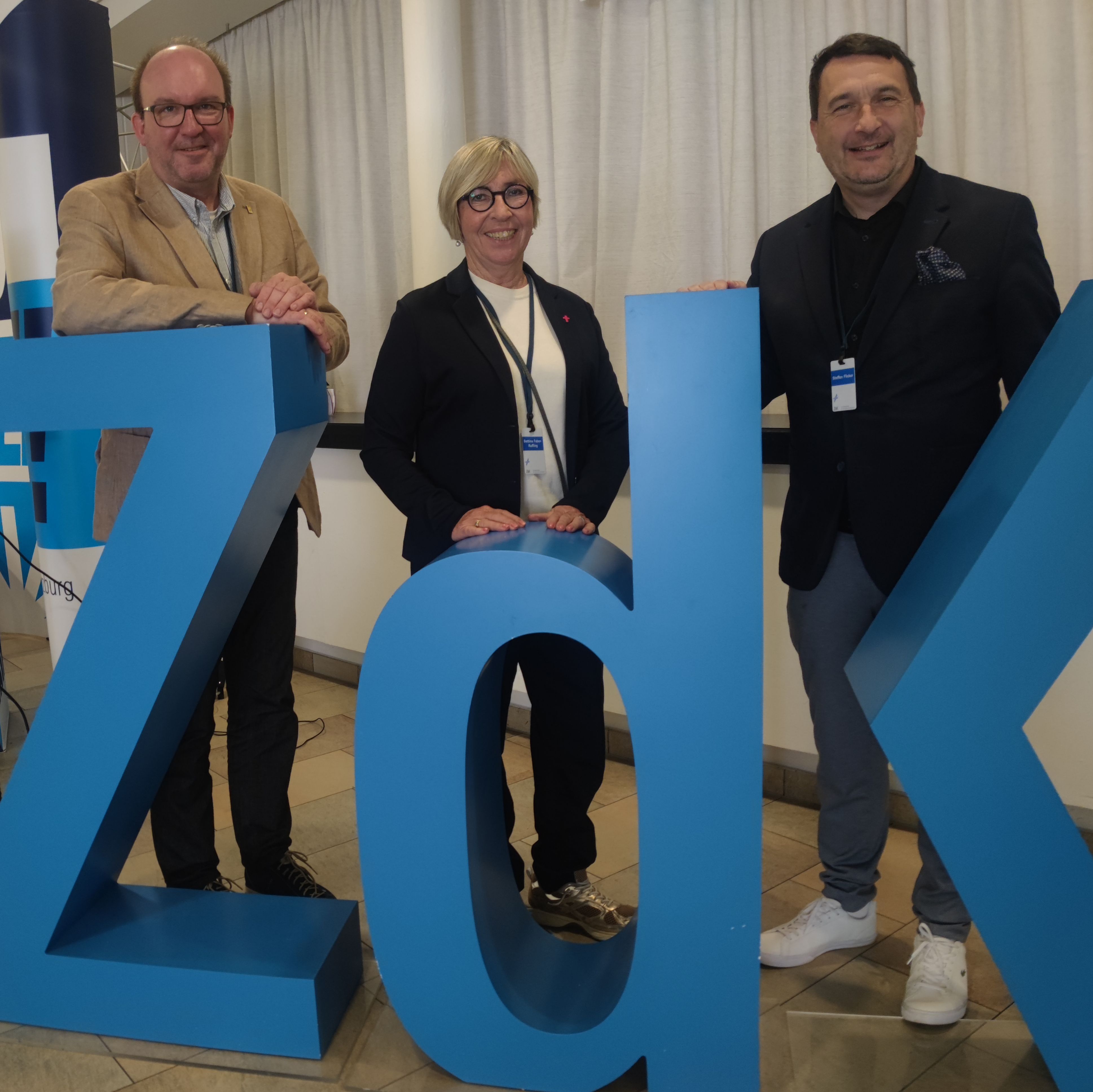 Auf dem Foto befinden sich von links nach rechts Marcus Leitschuh, Bettina Faber-Ruffing, Steffen Flicker. Diese stehen hinter einem aufgestellten ZdK-Logo.